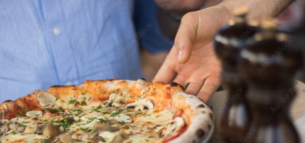A man's hand of a waiter serves a delicious vegetarian pizza with mushrooms to a client in a restaurant. Concept: favorite and popular food in the world. A man's hand of a waiter serves a delicious vegetarian pizza with mushrooms to a client in a restaurant. Concept: favorite and popular food in the world.