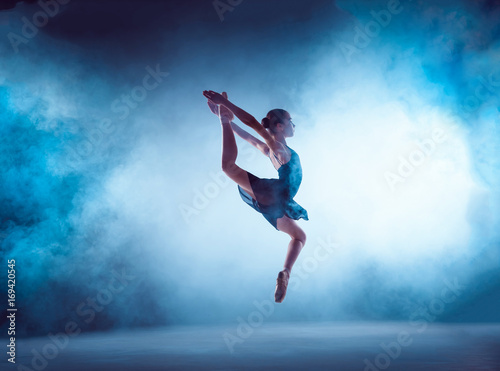 Beautiful young ballet dancer jumping on a lilac background.
