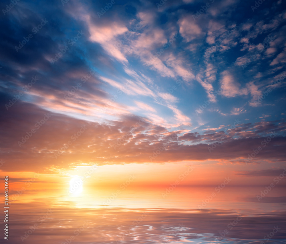 The fabulous sunset blue sky and the setting sun and clouds are reflected in the sea waves.