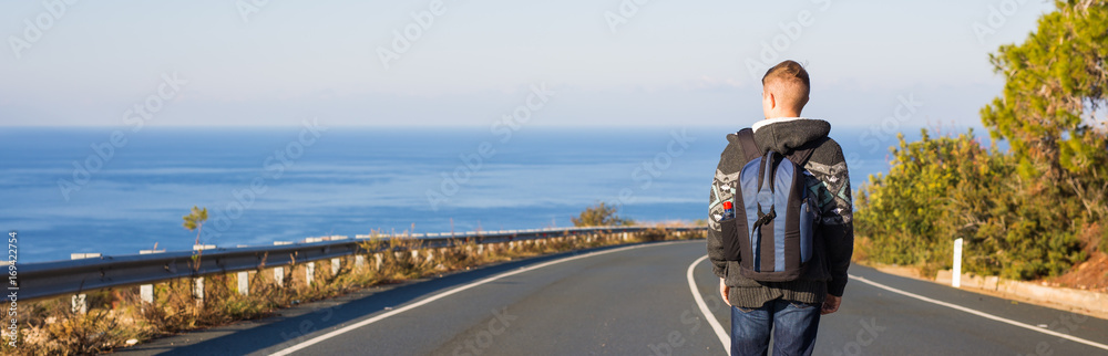Young man with backpack walks alone on a road. Travel, people and active life concept Young man with backpack walks alone on a road. Travel, people and active life concept