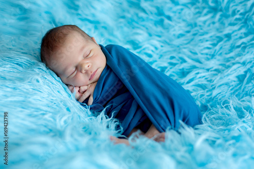 Cute baby boy, peacefully sleeping wrapped in blue wrap