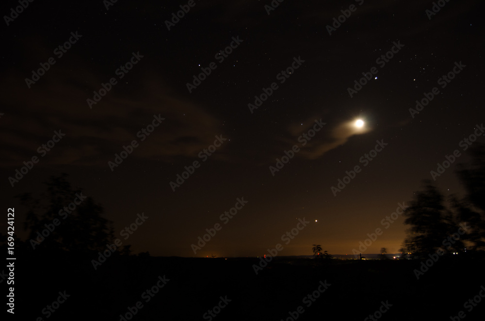Distant village lights visible under the moon, stars and clouds of o warm summer night near Heflin, Alabama, USA.