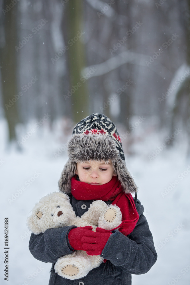 Sad lost child, boy in a forest with teddy bear, wintertime