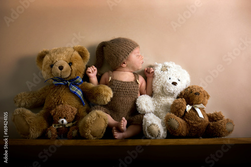 Newborn baby boy wearing a brown knitted bear hat and pants, sleeping on a shelf