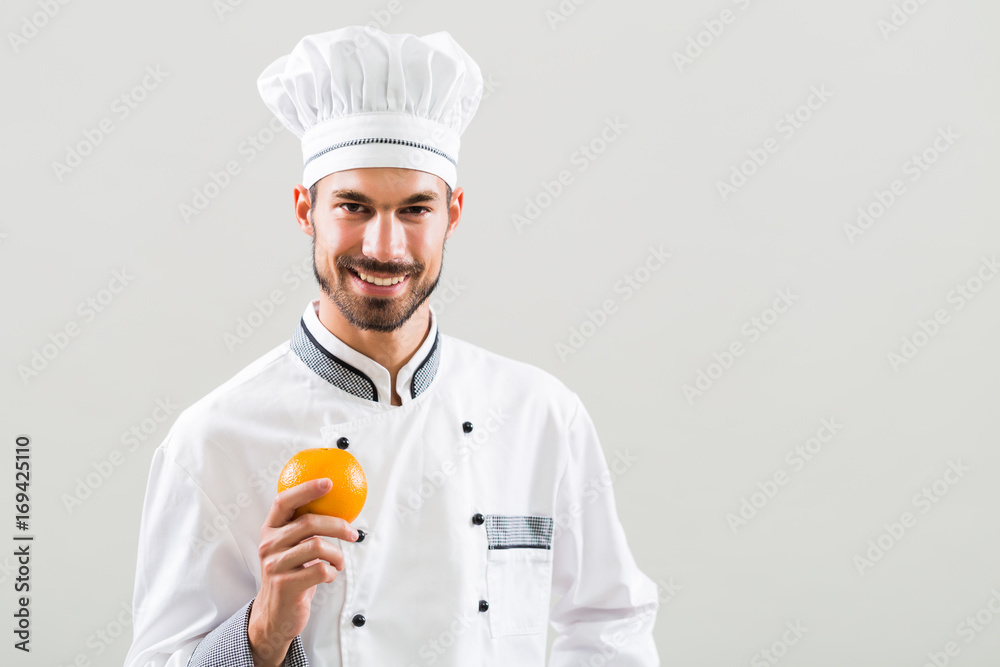 Chef is holding  orange on gray background.