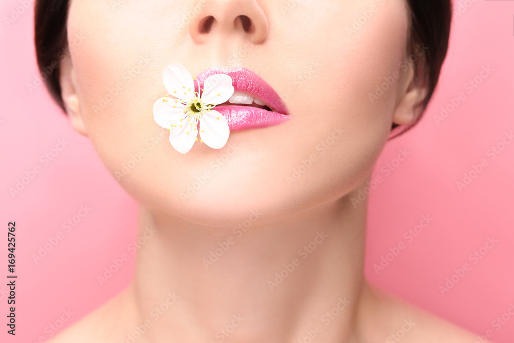 Beautiful young woman with flower between lips on color background