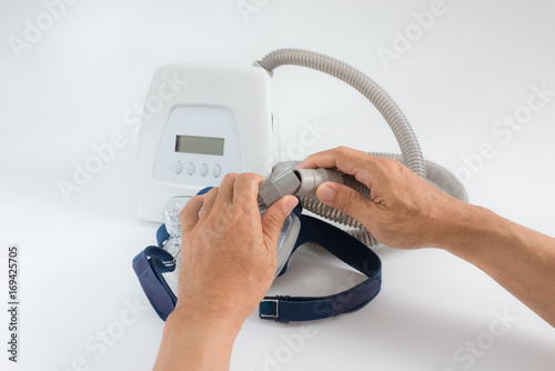 Man hands disassembly patient tube from a nasal mask ,white background,selective focus..Cpap Continuous positive airway pressure system includes of main unit,mask,patient tube and headgear. photo