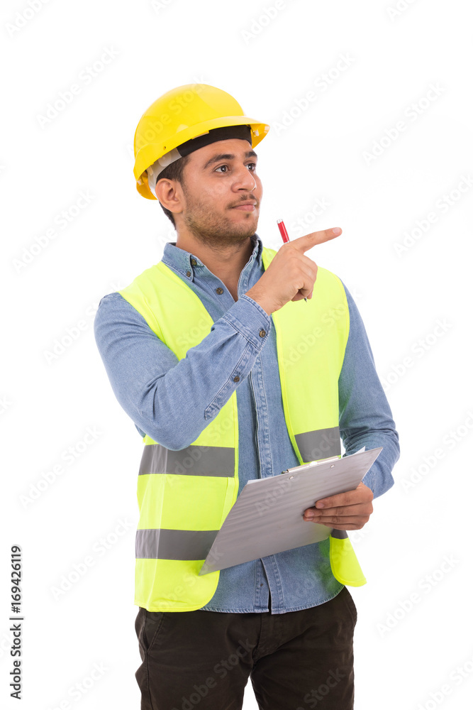 Happy young engineer holding a clipboard and pointing to something, guy wearing blue shirt and jeans with yellow vest and yellow helmet, isolated on white background Happy young engineer holding a clipboard and pointing to something, guy wearing blue shirt and jeans with yellow vest and yellow helmet, isolated on white background