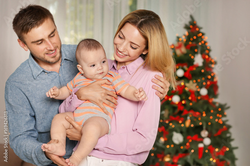 Happy parents with baby in decorated room for Christmas
