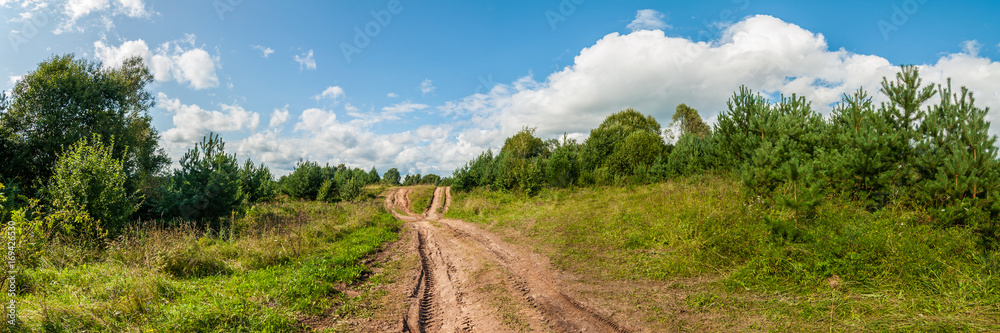 Panoramic view of a rural field road under a beautiful blue cloudy sky
