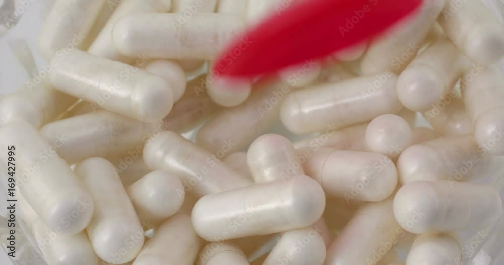 Close video of nicotinamide riboside capsules in a bowl being stirred with a red plastic spoon then selecting one pill.. Close video of nicotinamide riboside capsules in a bowl being stirred with a red plastic spoon then selecting one pill..