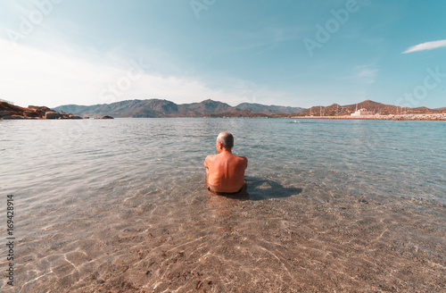 Aged man looking the horizon at the beach inside the water - Sardinia