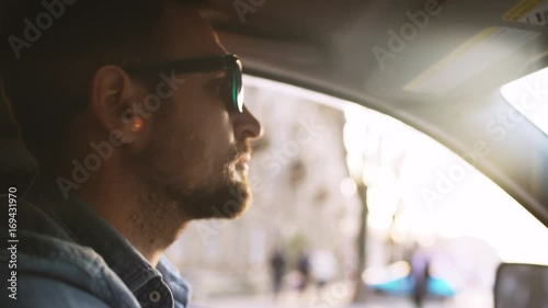Handsome man with beard in mirror sunglasses driving car in city with sunflare