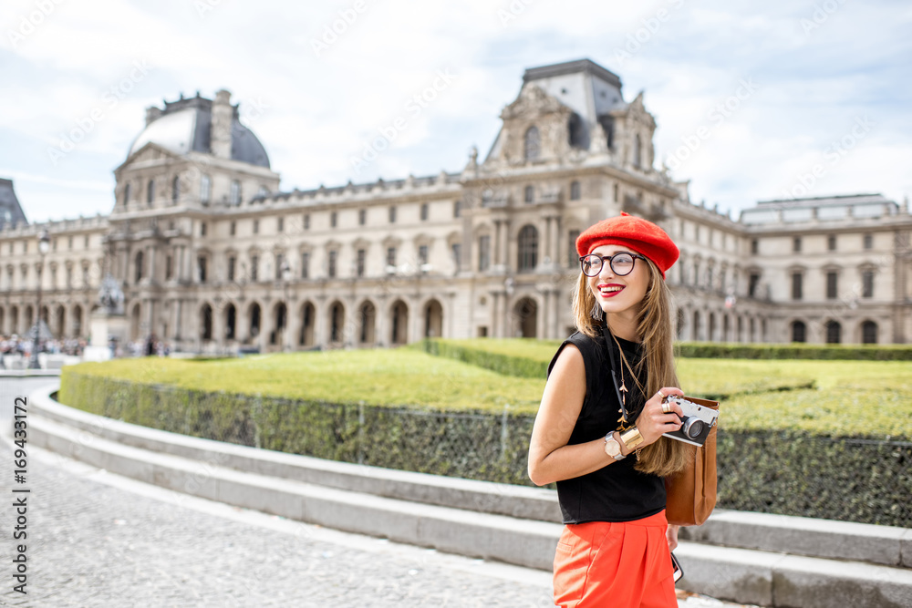 Obraz premium Young woman tourist in red cap walking with photo camera near the famous Louvre museum in Paris