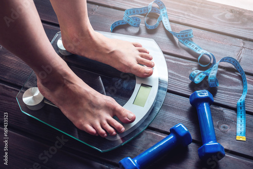 Fotografi Female feet standing on electronic scales, dumbbells and measuring tape
