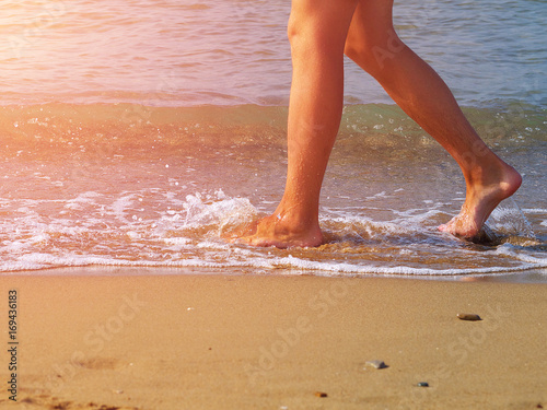 man's feet walking barefoot on beach by water edge, toned, sunlight effect