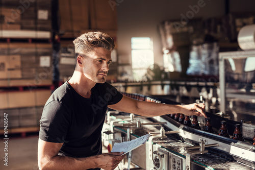 Young man supervising the process of beer bottling