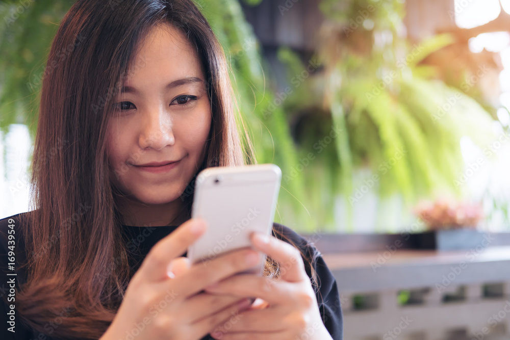 Closeup image of a beautiful Asian woman with smiley face using and looking at smart phone in modern cafe Closeup image of a beautiful Asian woman with smiley face using and looking at smart phone in modern cafe