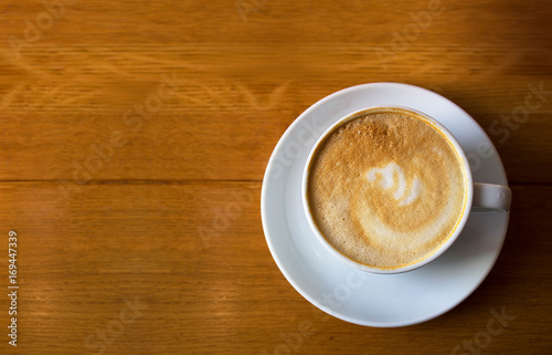 White cup of coffee on wooden table background, top view. Cappuccino latte in cafeteria