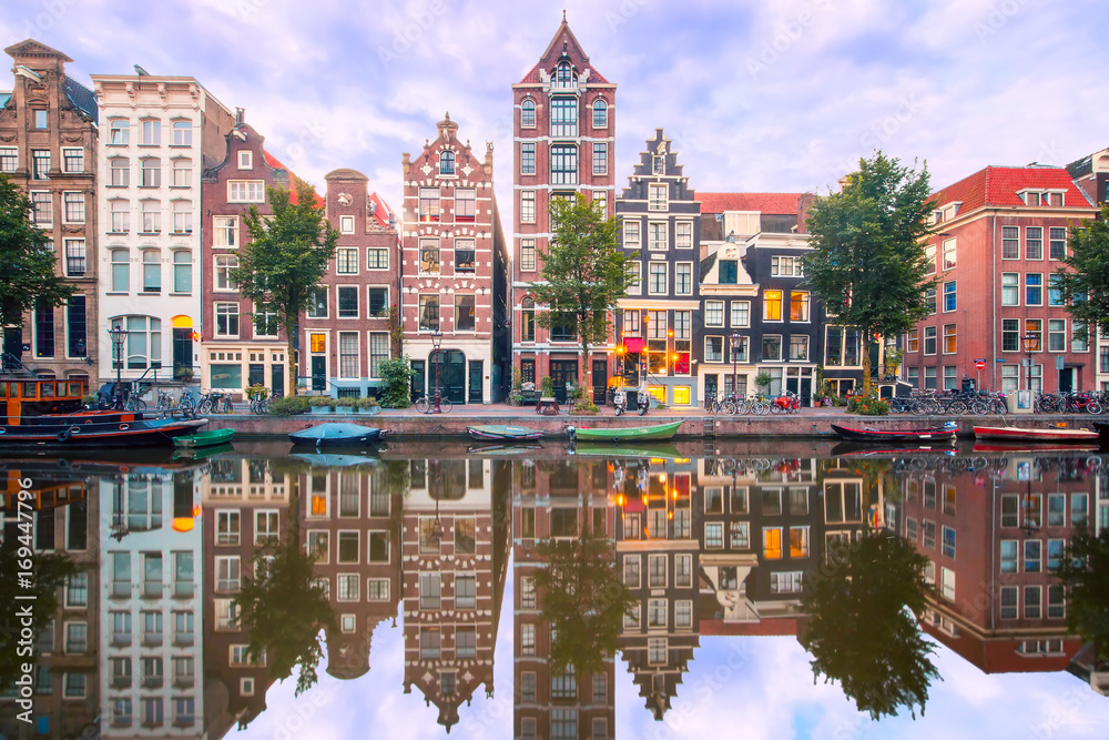 Naklejka premium Amsterdamski kanał Herengracht z typowymi holenderskimi domami i ich odbiciami podczas niebieskiej godziny porannej, Holandia, Holandia.