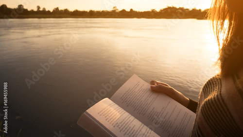 Close up hand of young woman reading the book at riverside in the evening.