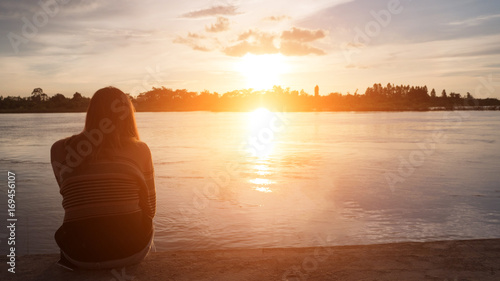 Young woman sitting alone at riverside in the evening.