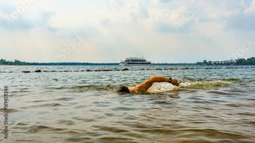 Man swimming in a lake with a boat in the background © DZiegler