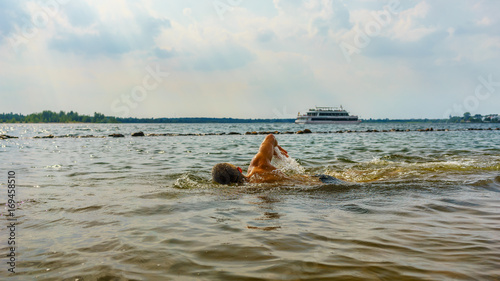Man swimming in a lake with a boat in the background © DZiegler