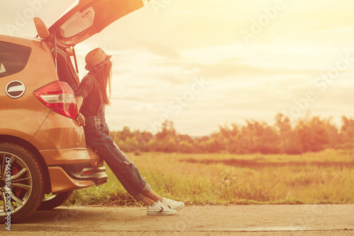 Hipster woman traveler sitting on hatchback car with nature background in vintage tone.She looking at the sky on sunset.