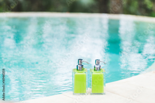 Two bottles of shampoo on edge of pool with turquoise and transparent clean water. Shower and spa kit in luxury hotel