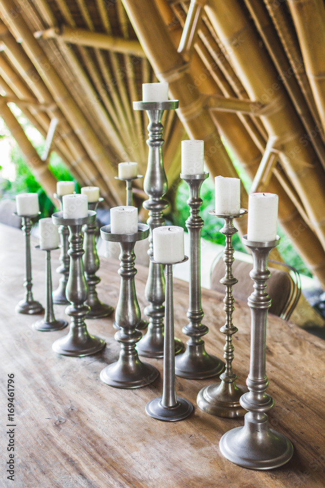 Many white candles in vintage metal candlesticks on wooden table as
