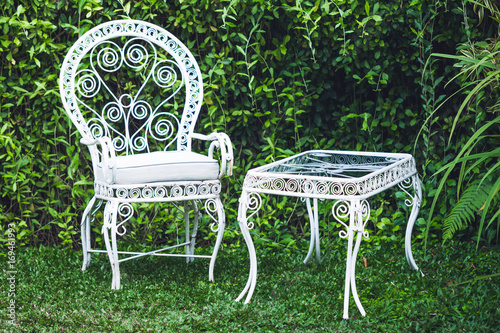 Old vintage furniture in garden with natural green background. White metal chair and table, old-fashioned european style
