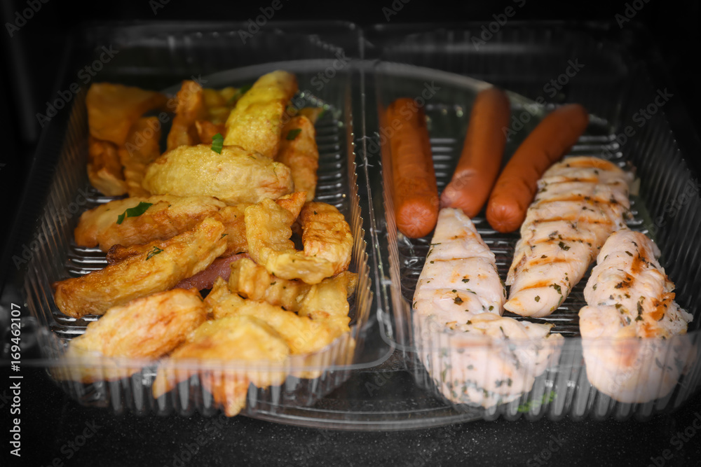 Container with fried potatoes, chicken meat and sausages in microwave oven