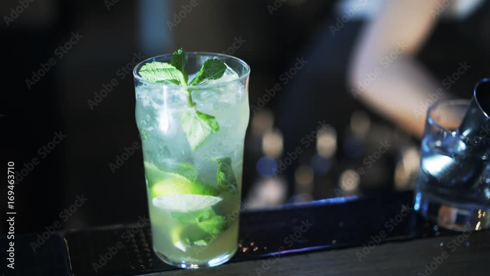Close up of an unrecognizable bartender putting some mint and a lime slice into a glass on the counter. Handheld real time close up shot Close up of an unrecognizable bartender putting some mint and a lime slice into a glass on the counter. Handheld real time close up shot