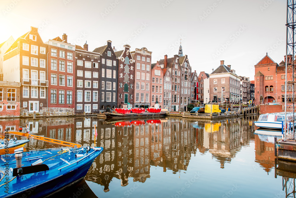 Morning view on the beautiful buildings and boats on the Damrak avenue in Amsterdam