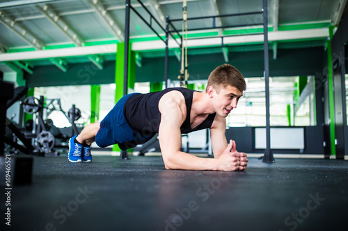 Young man workout in fitness club. Profile portrait of caucasian guy making plank or push ups exercise, training indoors