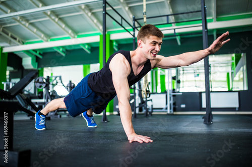 Confident muscled young man wearing sport wear and doing plank position while exercising on the gym interior