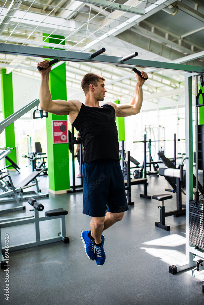 Fototapeta premium Shirtless muscular man doing ABS workouts on pull up bar in a gym.