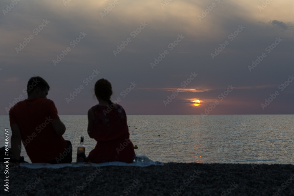 Silhouette of a couple sitting on the beach, watching the sunset