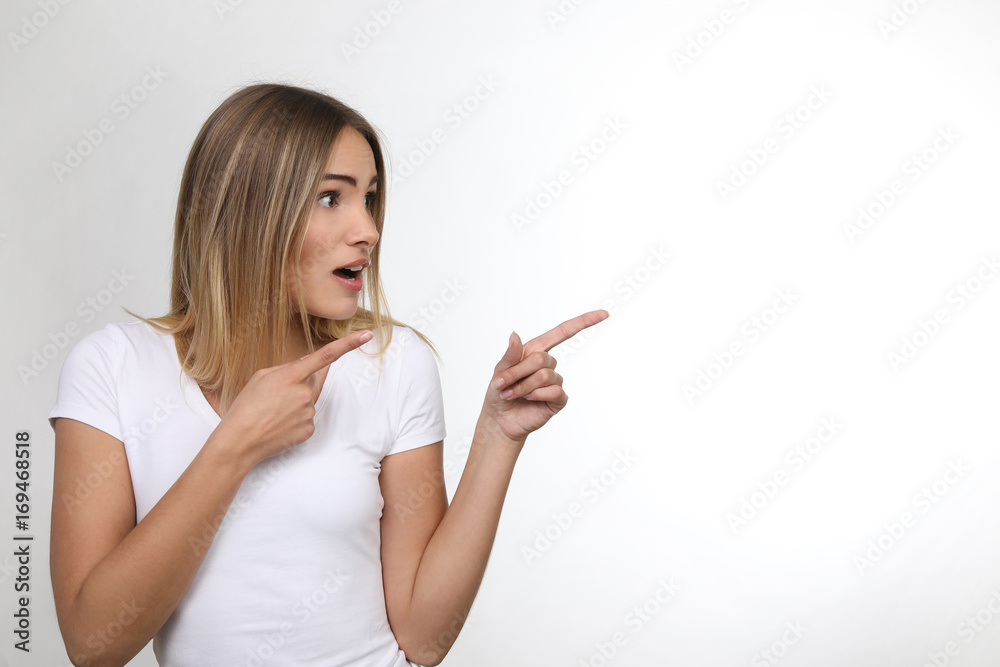 Hübsche blonde Frau schaut erstaunt und zeigt mit Fingern in eine Richtung Hübsche blonde Frau schaut erstaunt und zeigt mit Fingern in eine Richtung