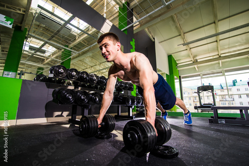 Strong, handsome man doing push-ups on dumbbells in a gym as bodybuilding exercise, training his muscles. Training.
