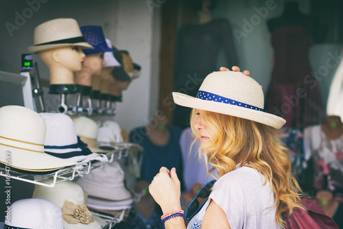 Canvas-taulu A young woman tourist choosing a hats in a shop