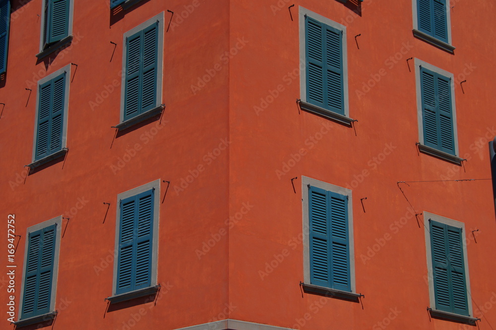 Dark orange facade of building with green wooden shutters closed.