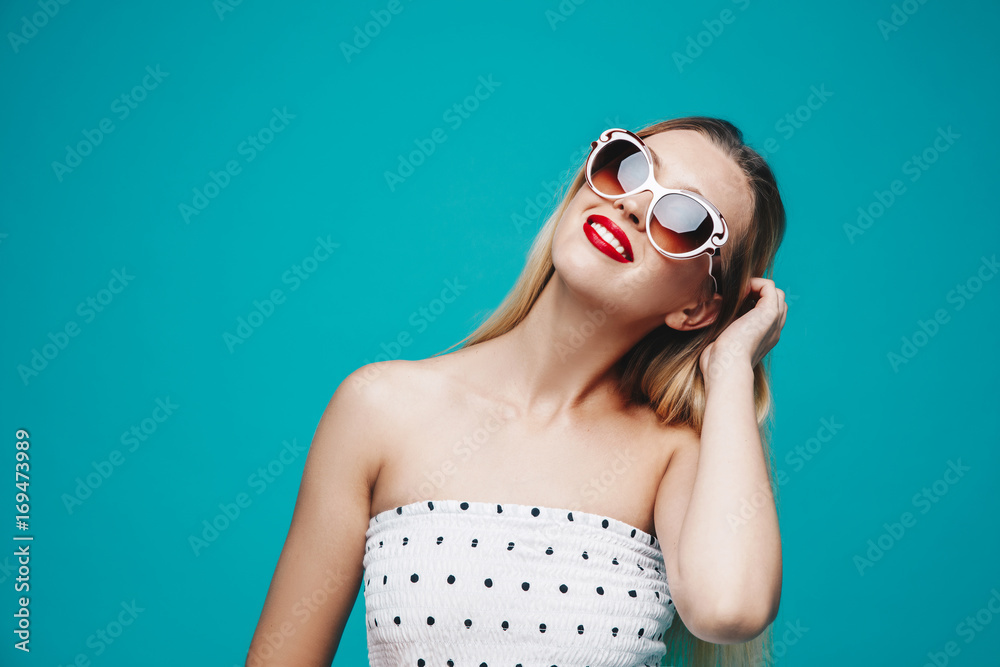 Summer model portrait. Dressed well stylish girl on sunglasses on blue turquoise background. Cheerful young woman on white dress. Summer model portrait. Dressed well stylish girl on sunglasses on blue turquoise background. Cheerful young woman on white dress.