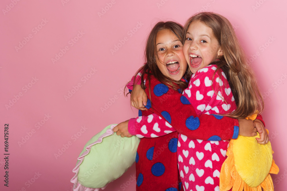 Girls in colorful polka dotted pajamas hold funny pillows - obrazy, fototapety, plakaty 
