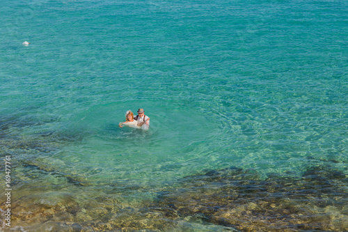 Happy couple swims after wedding in turquoise sea. Romantic newly-married couple enjoying a summer vacation.
