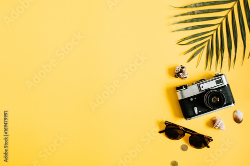 Flat lay traveler accessories on yellow background with palm leaf, camera and sunglasses. Top view travel or vacation concept. Summer background.