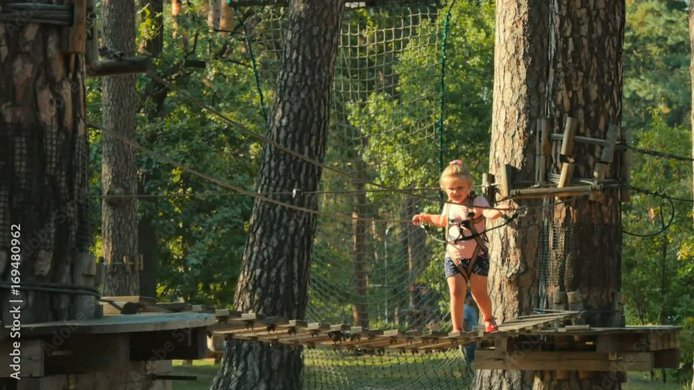 Little girl is going through a moving bridge in rope park Little girl is going through a moving bridge in rope park