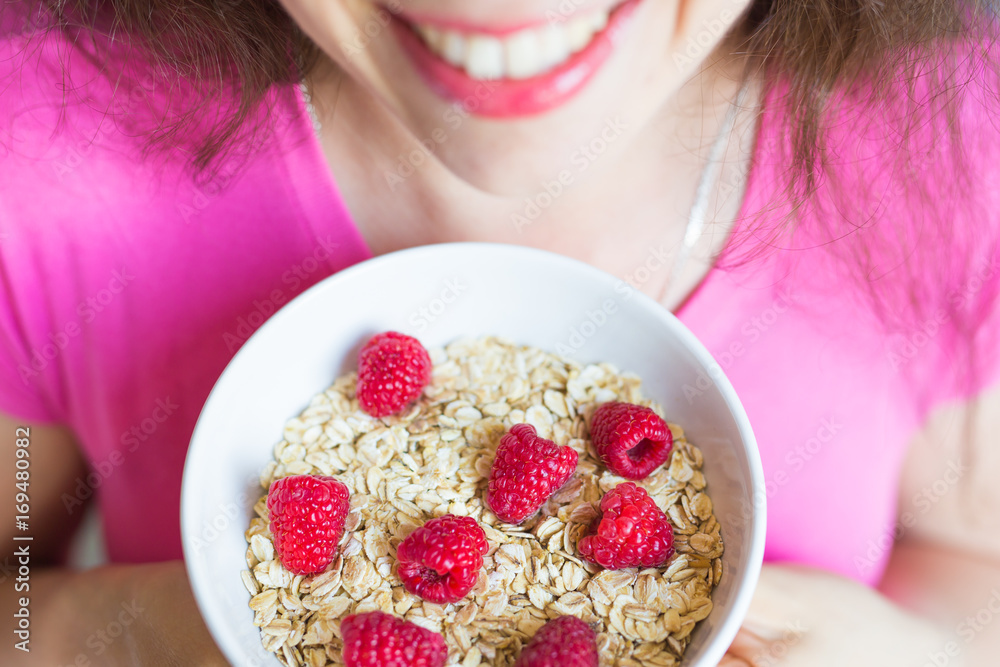 Woman's hands hold healthy and natural breakfast, oatmeal and raspberries in a bowl Woman's hands hold healthy and natural breakfast, oatmeal and raspberries in a bowl