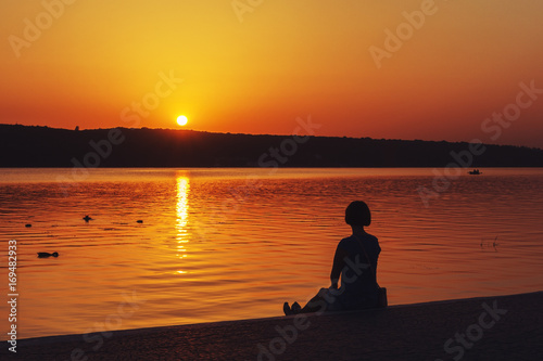The girl sits on the shore of a pool in the city and looks at the sunset.